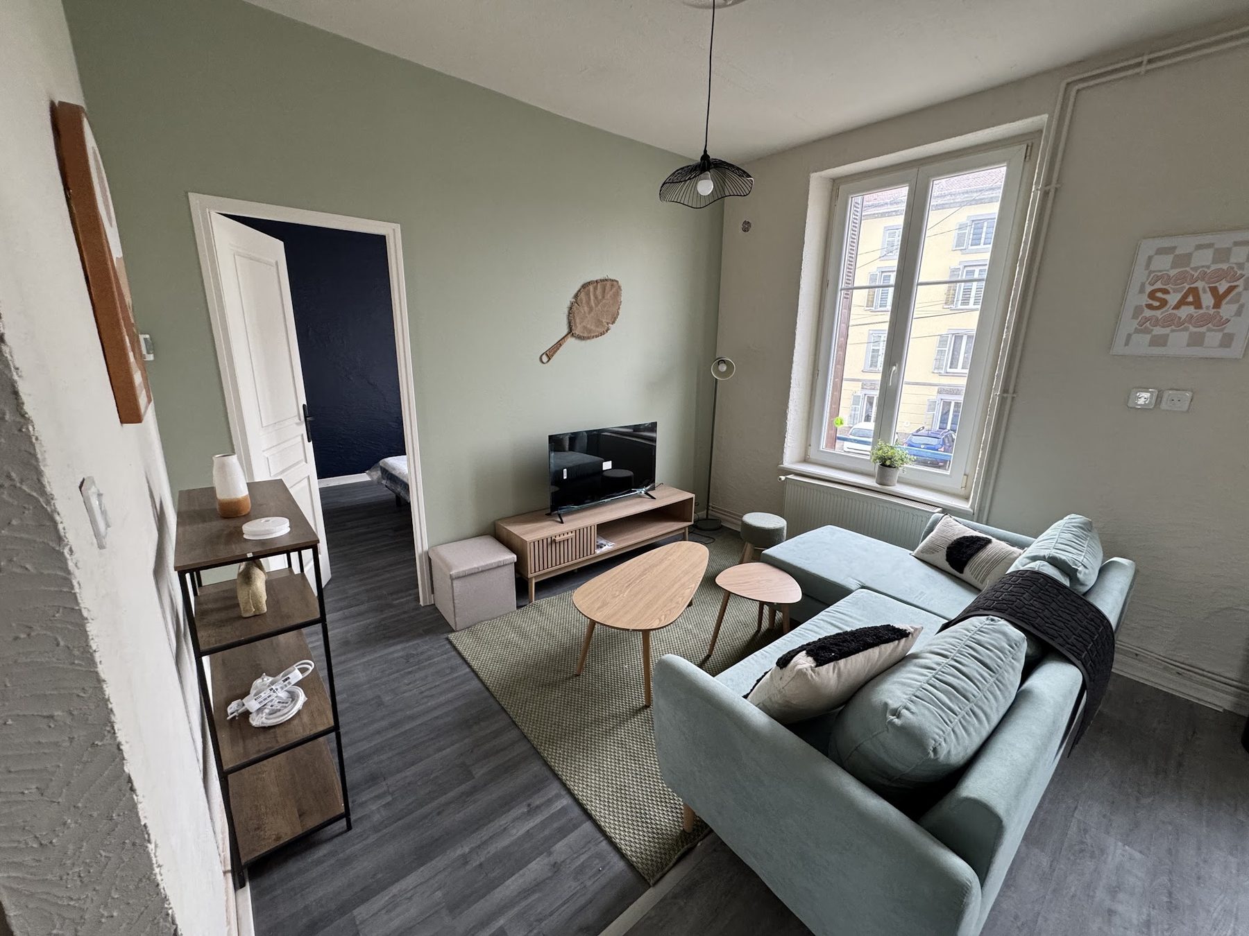 Séjour aux murs vert sauge, porte ouverte sur une chambre bleu nuit, sol gris